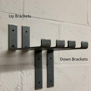 May include: A dark grey metal wall-mounted rack with five hooks, mounted on a white brick wall. The text "Up Brackets" and "Down Brackets" are visible.