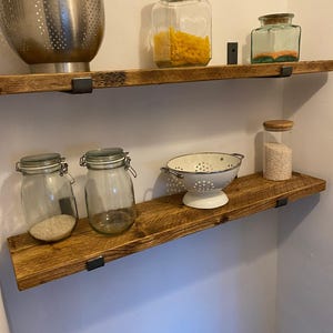 a set of wooden shelves with various kitchen items displayed on them, including a metal colander, glass jars, and a white strainer.