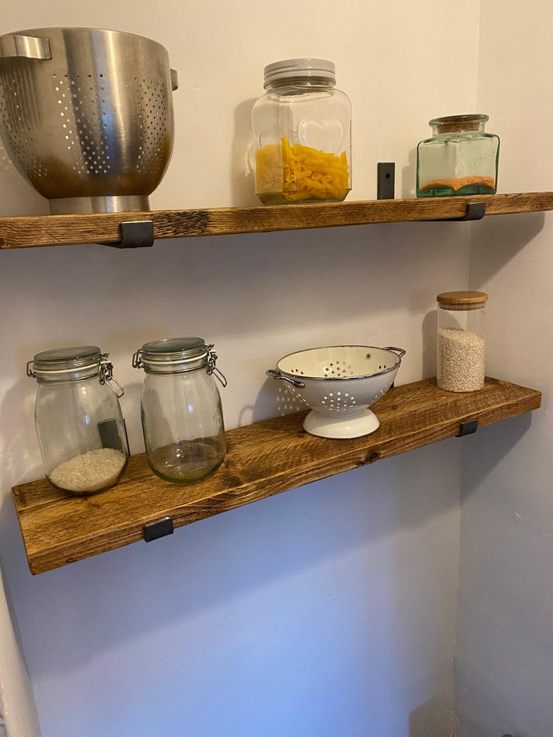 a set of wooden shelves with various kitchen items displayed on them, including a metal colander, glass jars, and a white strainer.