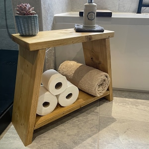 May include: A wooden bathroom shelf with a towel, toilet paper rolls, and a bottle of hand soap. The shelf is made of natural wood with a rustic finish.