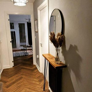 May include: A wooden console table with black hairpin legs sits in a hallway with a round mirror and dried flowers in a vase. The floor is a herringbone pattern.