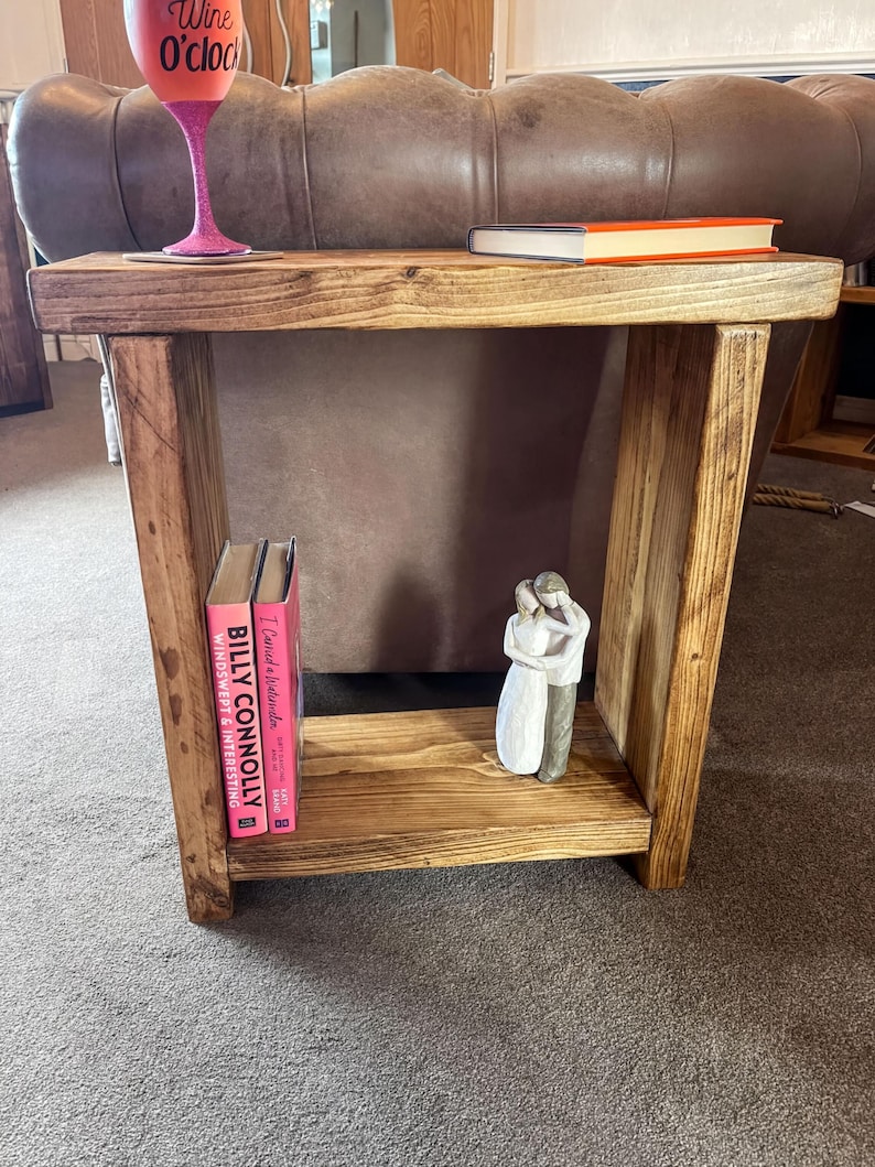 A wooden side table with a pink wine glass and a book on it, along with a small figurine of a couple.