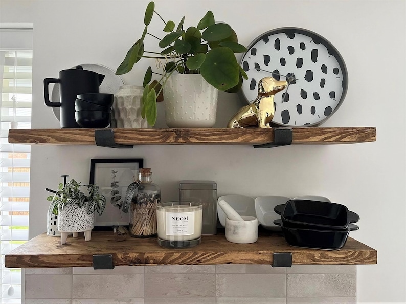 a wooden shelf with various decorative items and plants, including a black and white polka dot plate, a gold dog figurine, and a white vase with green leaves. The shelf also holds a black teapot, a white candle, and a white bowl.
