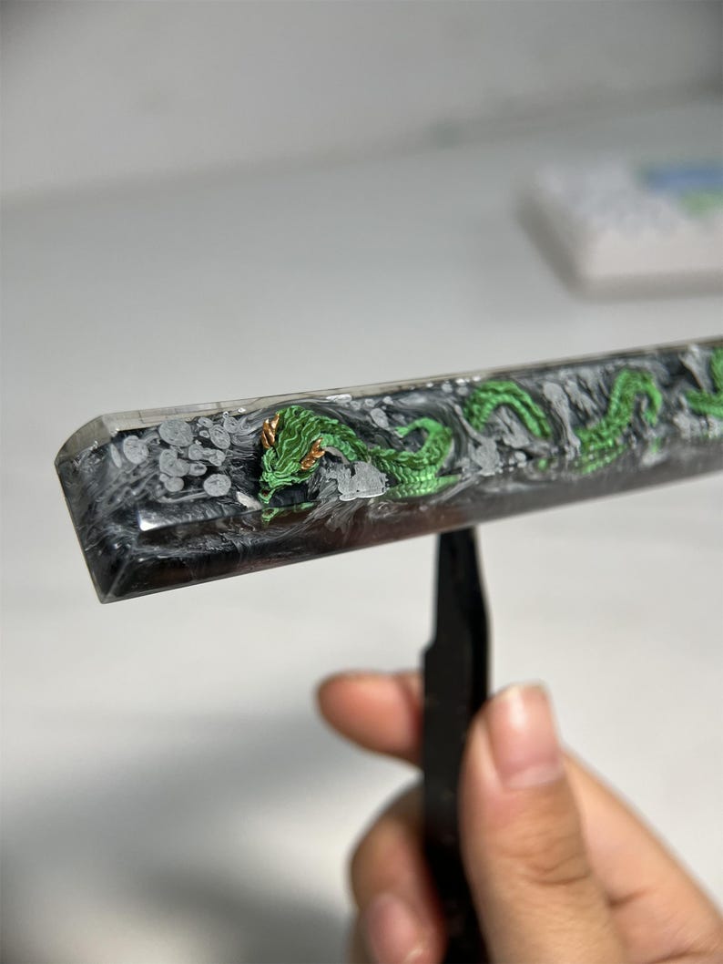 May include: A green dragon design is embedded in a clear resin keycap. The keycap is black and white with a swirling pattern.