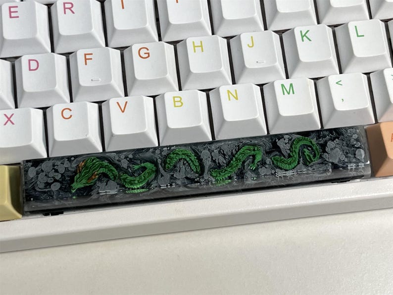 May include: A black and green keyboard keycap with a dragon design. The keycap is made of resin and has a glossy finish.