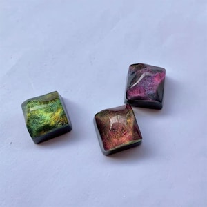 May include: Three square-shaped keycaps with iridescent finishes. The keycaps are green, purple, and red with a black base.
