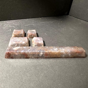 May include: A set of rectangular and square-shaped objects with a mottled brown and reddish-brown appearance. The objects are arranged on a dark grey surface, with a dark background. The objects appear to be made of a stone-like material.