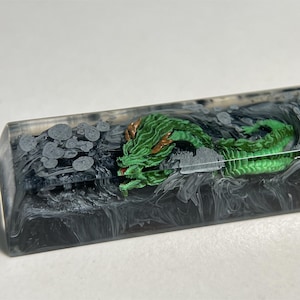 May include: A green dragon with gold accents is encased in clear resin with black and white swirls. The resin is in a rectangular shape.