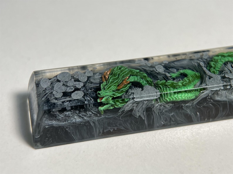 May include: A green dragon with gold accents is encased in clear resin with black and white swirls. The resin is in a rectangular shape.