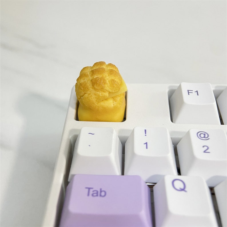 May include: A white keyboard with a yellow and brown pastry on the 'F1' key. The keyboard has purple keys for 'Tab' and 'Q'.