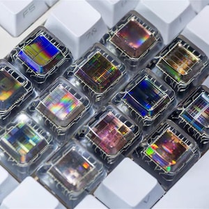 Può includere: Primo piano di una tastiera meccanica con tasti personalizzati. I tasti sono trasparenti con disegni iridescenti colorati, su uno sfondo di tasti bianchi. I tasti hanno un aspetto artistico unico.