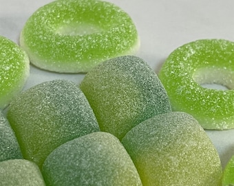 Op de afbeelding: Assortiment van groene gummy snoepjes in verschillende vormen, waaronder ringen en vierkanten. De snoepjes hebben een korrelige textuur en een lichtgroene kleur.