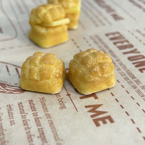 May include: Three miniature golden brown bread rolls with a shiny glaze. The rolls are on a brown paper surface with text that reads "Everyone Has Me".