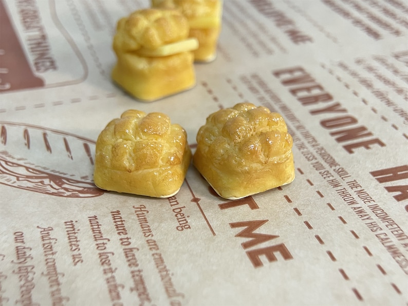 May include: Three miniature golden brown bread rolls with a shiny glaze. The rolls are on a brown paper surface with text that reads "Everyone Has Me".