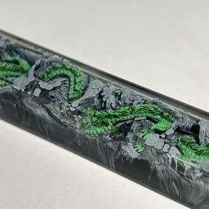 May include: A black and white resin keyboard keycap with a green dragon design.