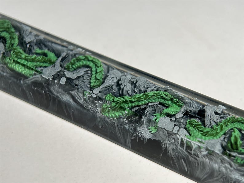 May include: A black and white resin keyboard keycap with a green dragon design.