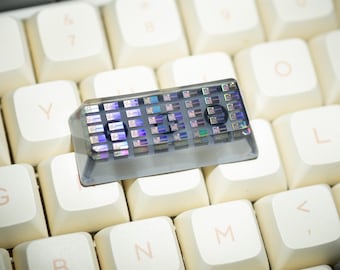 Può includere: Un copritasto personalizzato per tastiera con un design trasparente e iridescente, appoggiato su una tastiera color crema. Il copritasto mostra la parola "LED". È un accessorio unico per tastiere meccaniche.