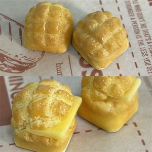 May include: Four miniature, golden brown,  bread rolls with a lattice pattern on top. Two of the rolls are plain and two are topped with a slice of yellow cheese.
