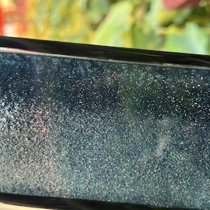 K&ouml;nnte beinhalten: Nahaufnahme einer dunkelblauen Oberfl&auml;che mit schimmerndem Glitzer, der in das Harz eingebettet ist. Der Glitzer ist eine Mischung aus Gold, Silber und Blau.