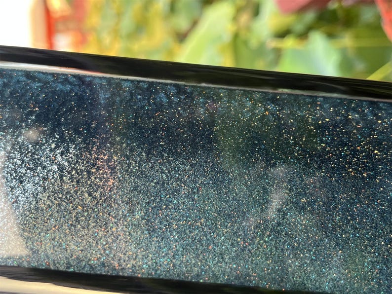K&ouml;nnte beinhalten: Nahaufnahme einer dunkelblauen Oberfl&auml;che mit schimmerndem Glitzer, der in das Harz eingebettet ist. Der Glitzer ist eine Mischung aus Gold, Silber und Blau.