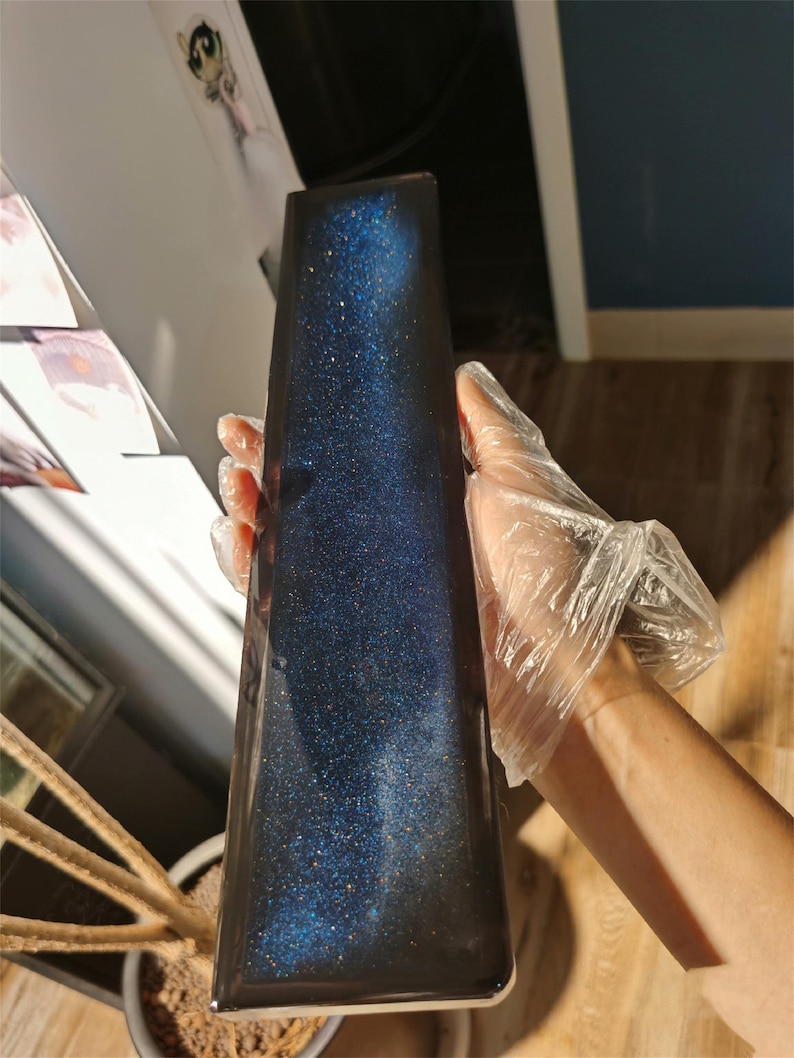 K&ouml;nnte beinhalten: Ein rechteckiges Harztablett in Dunkelblau mit glitzernder Oberfl&auml;che. Das Tablett hat ein galaktisches Aussehen mit einer Streuung von silbernem Glitter.