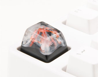May include: A black and white keycap with a red and white swirl design. The keycap is made of resin and has a glossy finish.