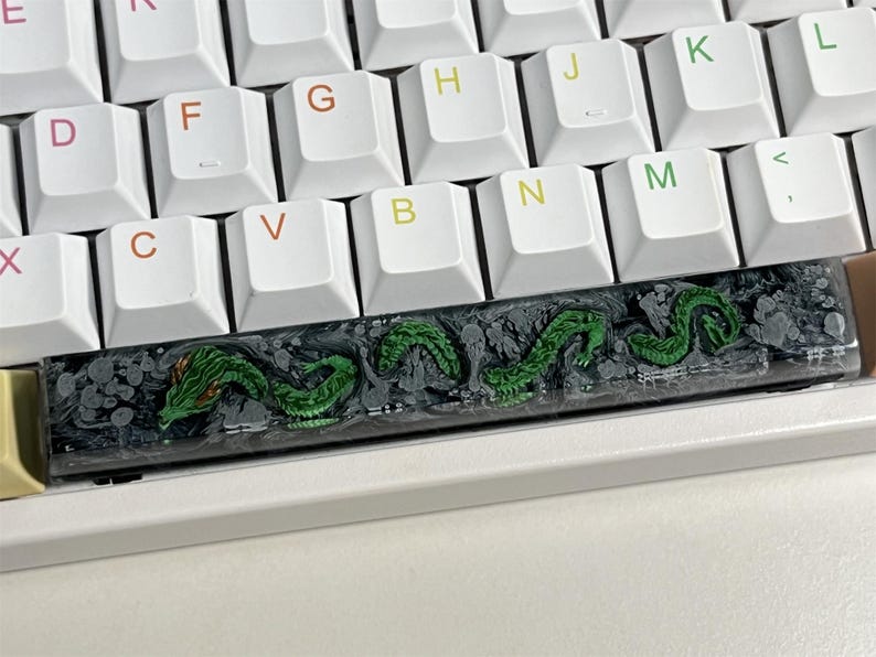 May include: A black and green keyboard keycap with a dragon design. The keycap is made of resin and has a textured surface.