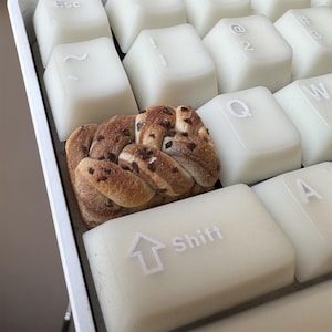 May include: A close-up of a white keyboard with a chocolate swirl pastry resting on the "Shift" key. The pastry is a light brown color with dark brown chocolate swirls.