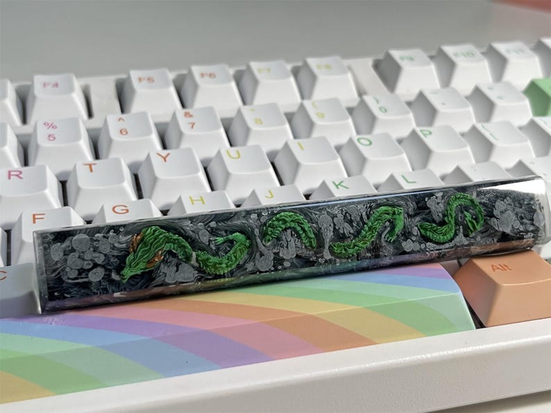 May include: A black and green keyboard keycap with a swirling design and a green dragon motif.
