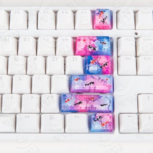Peut inclure: Un clavier blanc avec des touches colorées. Les touches sont rectangulaires et ont un design marbré rose, bleu et blanc. Les touches sont disposées en rangée sur le clavier.