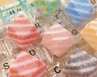 Op de afbeelding: Assortiment van kleurrijke, gestreepte, ruitvormige snoepjes gerangschikt op een transparant plastic toetsenbord. De snoepjes zijn wit, roze, rood, groen, blauw en grijs.