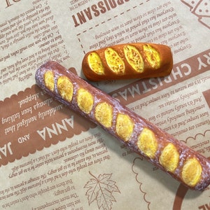 May include: Two long, brown, crusty bread rolls with a yellow filling. The rolls are on a brown paper background with text that says "Merry Christmas".