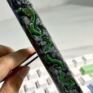 May include: A clear resin keycap with a green dragon design and black and white swirls. The keycap is on a white keyboard.