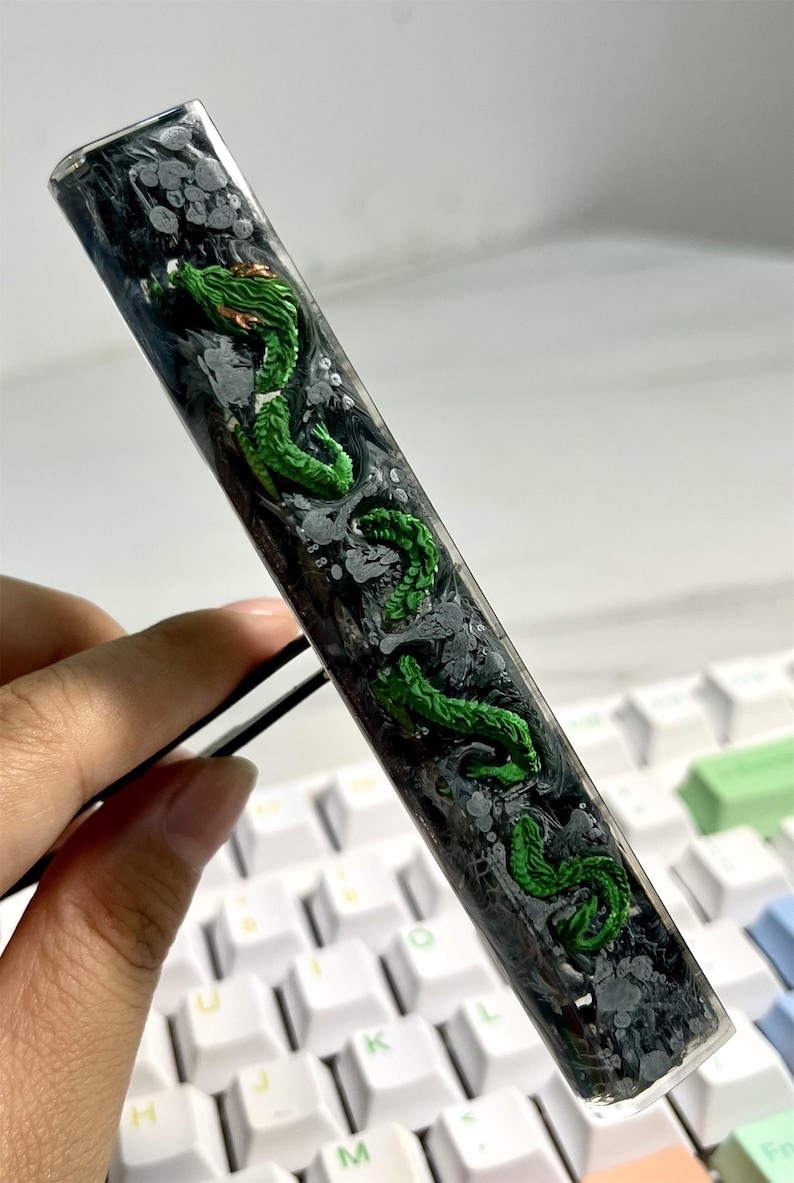 May include: A clear resin keycap with a green dragon design and black and white swirls. The keycap is on a white keyboard.