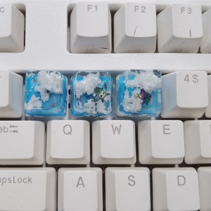May include: Three blue and white keycaps with different designs. The keycaps feature a cloud design with a butterfly, a star, and a flower.