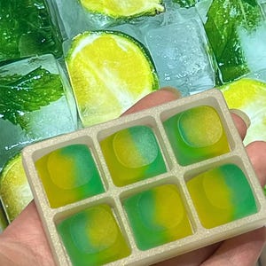 May include: A rectangular white tray containing six square-shaped resin keycaps, each featuring a gradient blend of vibrant yellow and green colours. The keycaps have a smooth, semi-translucent finish and are arranged in two rows of three.