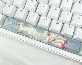 Op de afbeelding: Een wit toetsenbord met een aangepaste toetsdop met een witte vos met rode accenten op een blauwe en witte achtergrond.