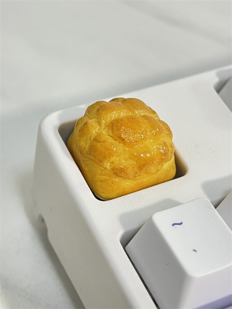 May include: A close-up of a yellow and brown bread-shaped keycap on a white keyboard.