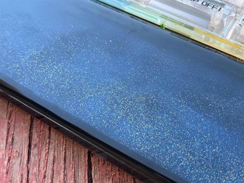 K&ouml;nnte beinhalten: Nahaufnahme einer dunkelblauen Oberfl&auml;che mit einer feinen Schicht Glitzer. Die Oberfl&auml;che ist glatt und reflektierend, mit einem leichten Glanz.