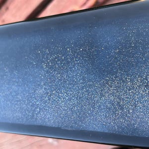K&ouml;nnte beinhalten: Nahaufnahme einer dunkelblauen Oberfl&auml;che mit einer feinen Schicht Glitzer. Der Glitzer ist silbern und erzeugt einen funkelnden Effekt.