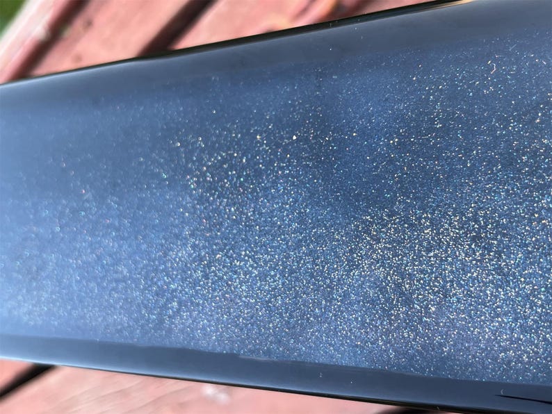 K&ouml;nnte beinhalten: Nahaufnahme einer dunkelblauen Oberfl&auml;che mit einer feinen Schicht Glitzer. Der Glitzer ist silbern und erzeugt einen funkelnden Effekt.