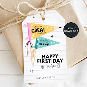 May include: A rectangular gift tag with a white lined paper background featuring two pennant flags, one yellow and one teal, with the text "here is to a GREAT school year!", "Hip Hip hooray!", "HAPPY FIRST DAY of school!", and "PAISLEY GREEN".