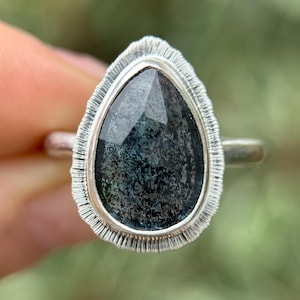 May include: A silver ring featuring a pear-shaped dark green gemstone set in a textured silver bezel.