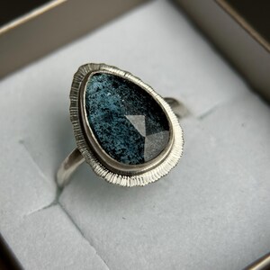 May include: A silver ring featuring a teardrop-shaped blue gemstone set in a textured silver bezel.