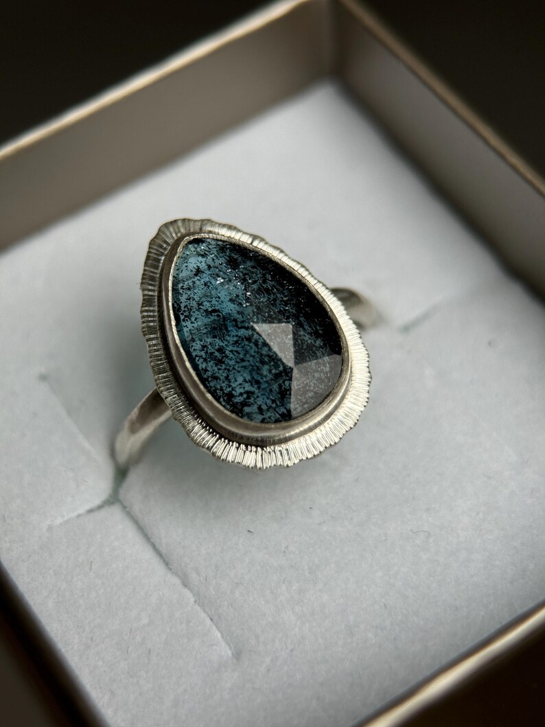 May include: A silver ring featuring a teardrop-shaped blue gemstone set in a textured silver bezel.