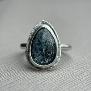 May include: A silver ring featuring a teardrop-shaped blue gemstone set in a textured silver bezel.