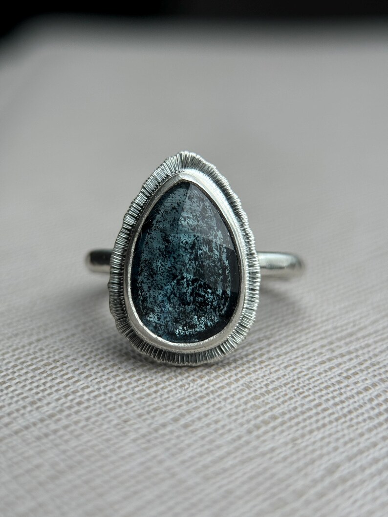 May include: A silver ring featuring a teardrop-shaped blue gemstone set in a textured silver bezel.