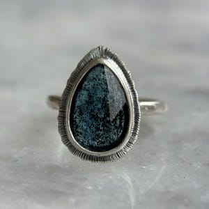 May include: A silver ring featuring a teardrop-shaped blue gemstone set in a textured silver bezel.