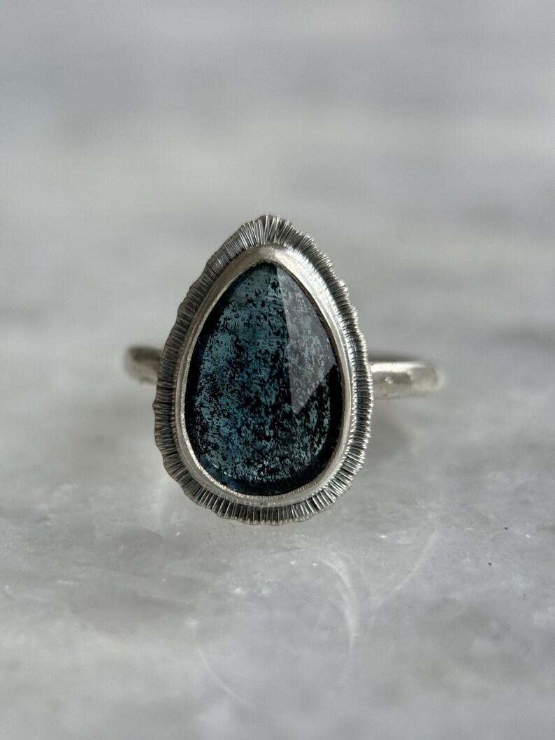 May include: A silver ring featuring a teardrop-shaped blue gemstone set in a textured silver bezel.