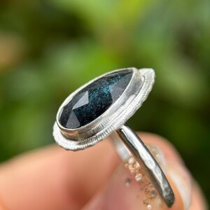 May include: A silver ring featuring a pear-shaped dark green gemstone set in a bezel setting. The ring has a textured band.